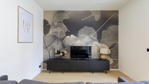 Un salon moderne avec un meuble TV en bois foncé, un téléviseur à écran plat et une œuvre d’art murale représentant de grandes feuilles.