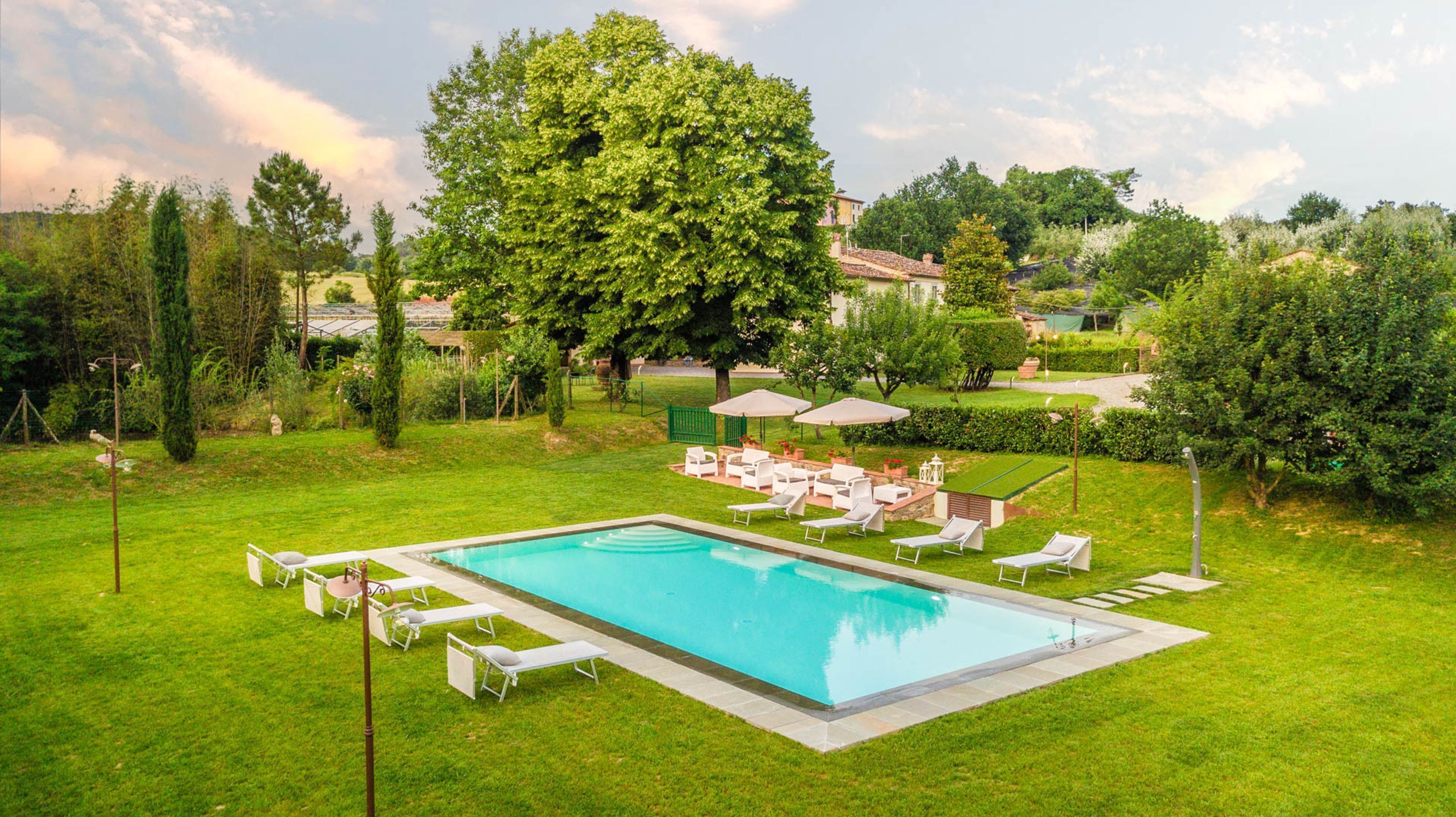 Una piscina rectangular amb gandules i ombrel·les, envoltada per gespa i arbres ben cuidats.