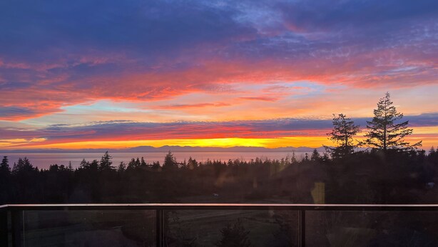 Sonnenuntergangblick von einem Balkon mit Glasgeländer, mit Blick auf eine bewaldete Landschaft und entfernte Berge.