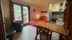 Une pièce compacte comprenant un lit, une table à manger, une chaise, un petit coin cuisine et une vue sur l’extérieur.