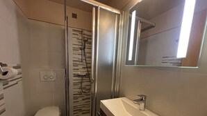 Une salle de bain moderne avec une douche à parois de verre, des toilettes blanches et un lavabo surmonté d’un miroir.