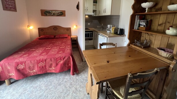 Une chambre avec un lit, des tables de chevet et une table à manger en bois avec des chaises. Il y a également un coin cuisine avec des placards et un évier.