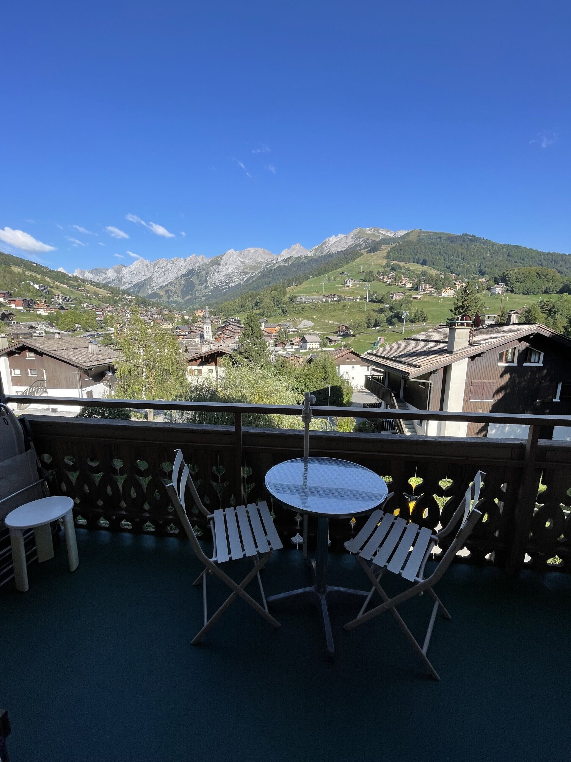 Un balcon avec une table et des chaises, donnant sur un paysage montagneux parsemé de bâtiments.