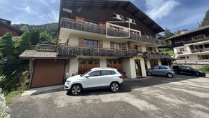 Un immeuble à plusieurs étages doté de balcons, d’un espace de stationnement et surplombant un paysage montagneux.