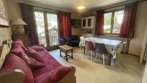 Una sala de estar con sofá, una mesa de comedor con sillas, una lámpara y una ventana con cortinas.