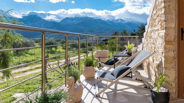 Un balcón con vistas a montañas nevadas, un muro de piedra y mobiliario exterior.