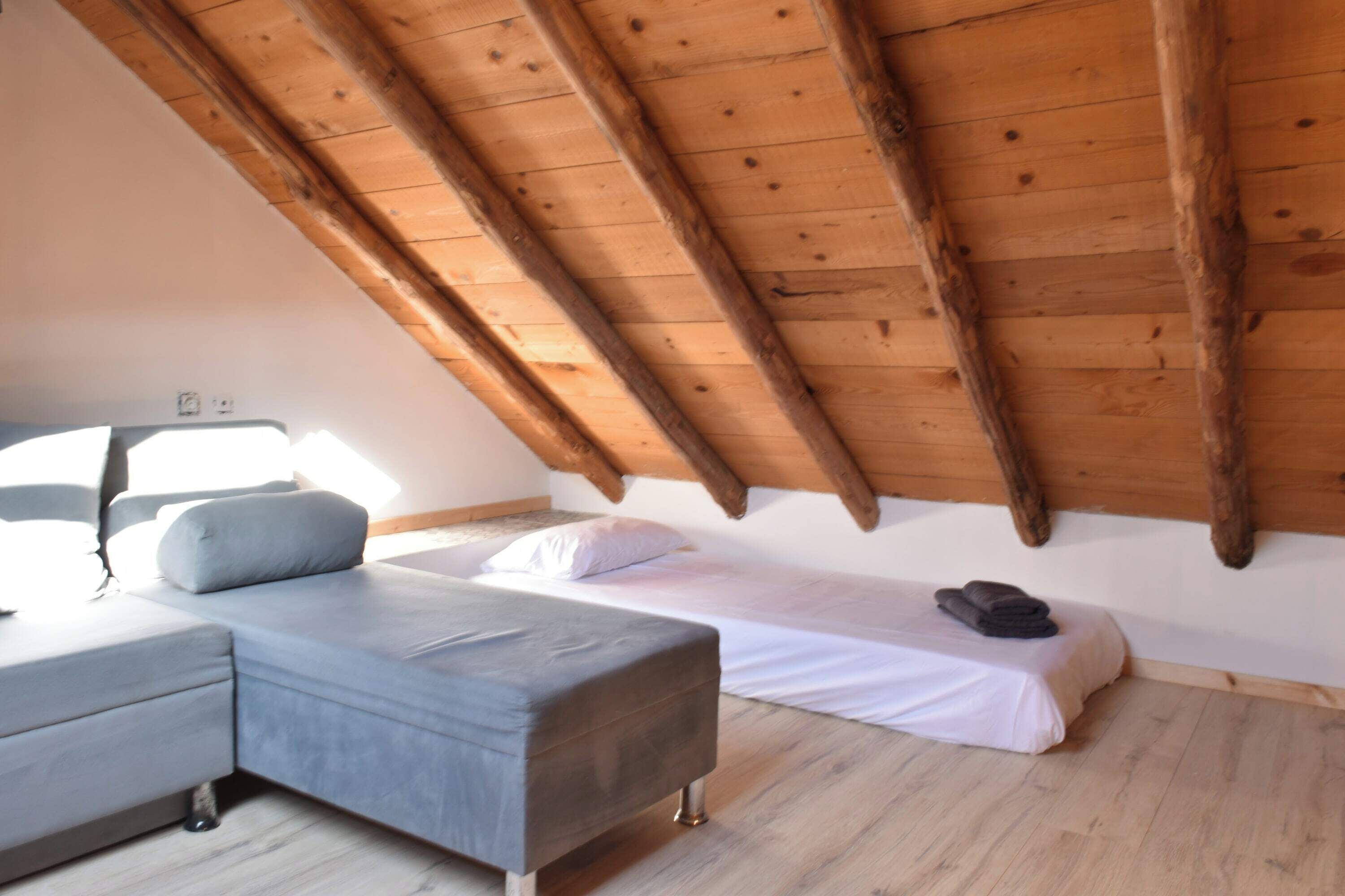 A bedroom with a sloped ceiling, a bed, a bench, and a small table.