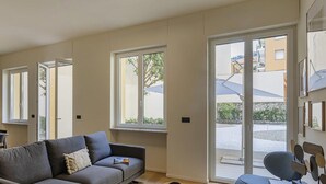 A modern living room with a grey sofa, a blue chair, and a large window providing a view of the outside. - Riviera Flavour Apartments by Wonderful Italy - Olivo (Santa Margherita Ligure)