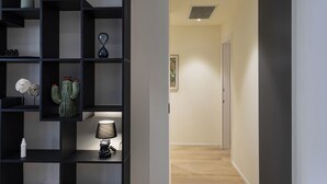 A modern interior with a black shelving unit displaying various decorative items, a hallway with wooden flooring, and a door at the end. - Riviera Flavour Apartments by Wonderful Italy - Olivo (Santa Margherita Ligure)