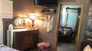 A bedroom with a bed, a dresser, a mirror, a television, and a small round ottoman. - Lush Couples Cottage w/ access to Waterfront Property, pier, pool & hot tub (Bacliff)