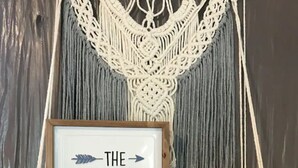 A macrame wall hanging with a framed sign that reads "THE Adventure BEGINS". - Lush Couples Cottage w/ access to Waterfront Property, pier, pool & hot tub (Bacliff)