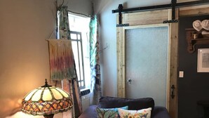A cozy living room with a dark brown sofa, a small round table with a lamp, and a colorful tapestry. - Lush Couples Cottage w/ access to Waterfront Property, pier, pool & hot tub (Bacliff)