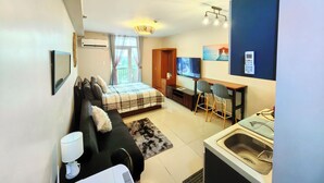 Une chambre d’hôtel de taille réduite, équipée d’un lit, d’un bureau, d’une télévision et d’une kitchenette.