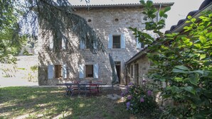A stone building with a courtyard, a table with chairs, and a garden with purple flowers.