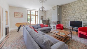 A living room with a large grey sectional sofa, a wooden coffee table, a red armchair, a television, and a stone wall.