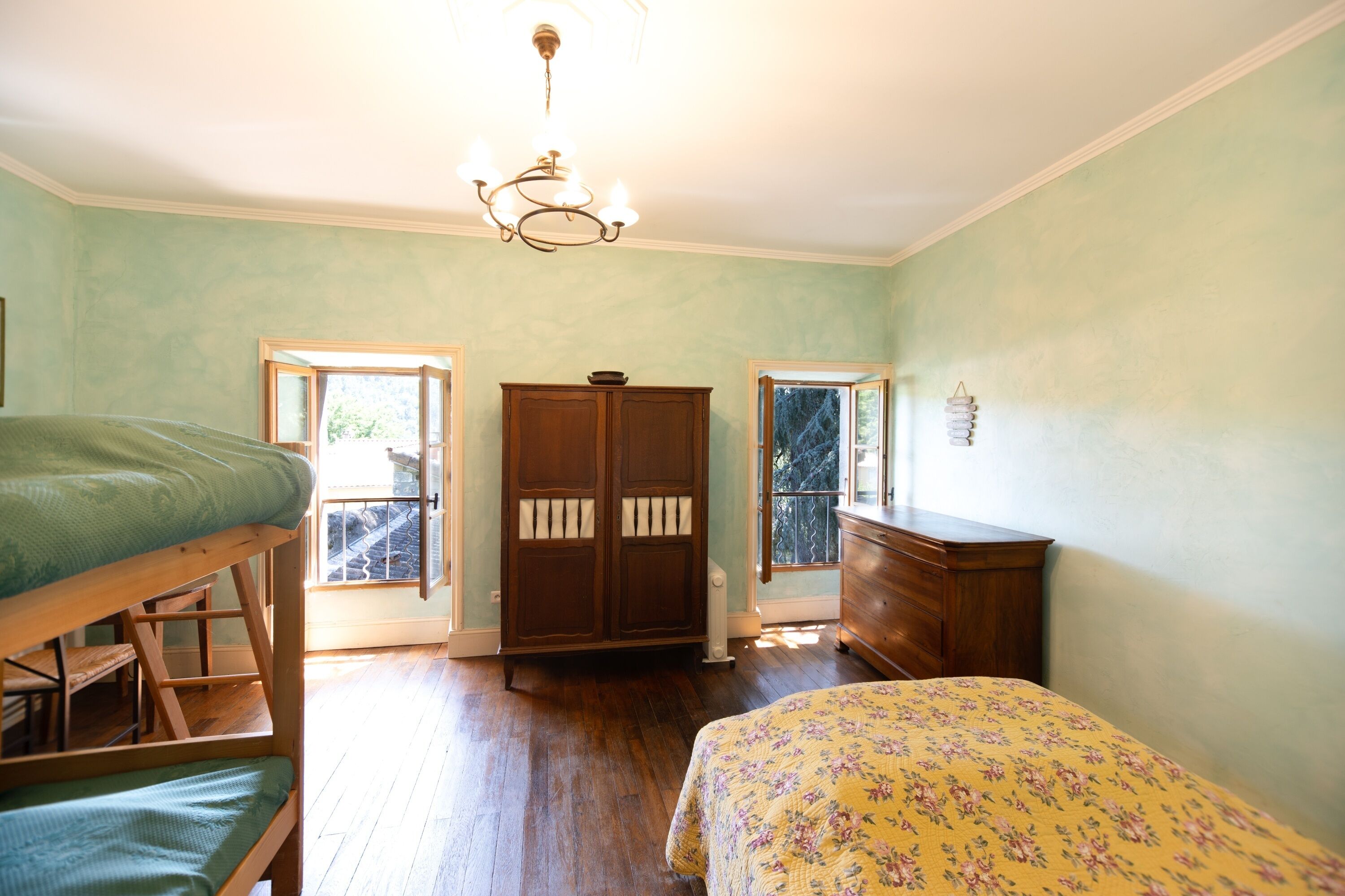 A bedroom with a bunk bed, a dresser, a wardrobe, and a window with a view.