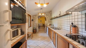 A kitchen with a microwave, stove, and wooden cabinets. There is a stone wall and a tiled backsplash.