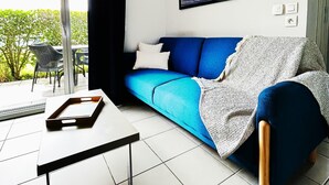 Un salon moderne avec un canapé bleu, une porte vitrée donnant sur un espace extérieur, un tableau encadré au mur et une petite table avec un plateau.