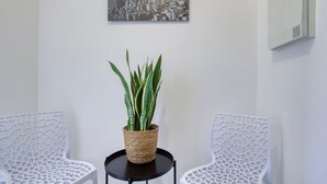 A room with two white chairs, a small round table with a woven plant pot, and a cityscape picture on the wall.
