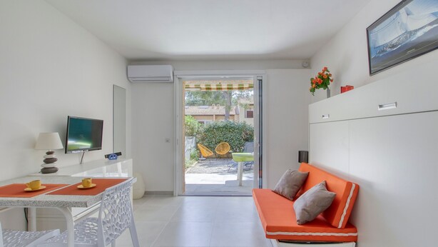A modern room with a dining table, chairs, a sofa, a TV, and a sliding glass door leading to an outdoor area with chairs and a table.