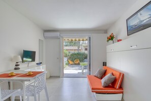 Ein modernes Zimmer mit Esstisch, Stühlen, einer Couch, einem Fernseher und einer Glastür, die zu einem Außenbereich mit Stühlen und Tisch führt.