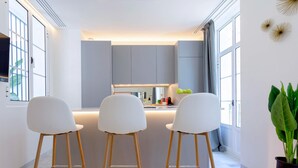 A modern kitchen with a central island, three white bar stools, and a potted plant. - Genteel Home Catedral III (Cadiz)