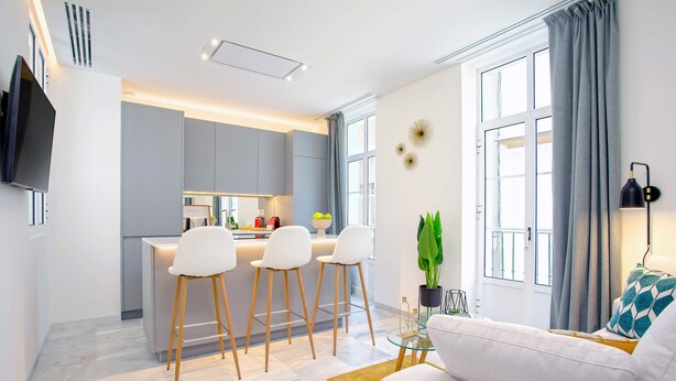 A modern living room with a sofa, a coffee table, and a kitchen area with bar stools. - Genteel Home Catedral III (Cadiz)