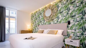 A large bed with white linens, a round mirror above it, and a wall with a leafy pattern. - Genteel Home Catedral III (Cadiz)