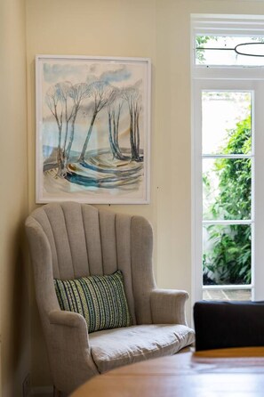 A room with a chair, a painting, and a window with greenery outside.