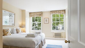 A bedroom with a large bed, two windows with curtains, a radiator, and a door with a knob.