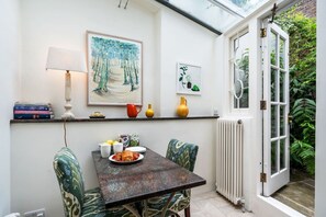 A dining area with a table set for two, a lamp, and artwork on the wall.