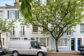 Een zilveren busje geparkeerd voor een rij witte en blauwe herenhuizen met balkons.