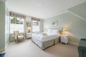 Een slaapkamer met een groot bed, nachtkastjes, een stoel, een bureau en een raam met gordijnen.