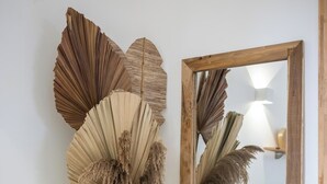 A room with a large mirror, a white vase with dried plants, a wooden stool, and a bed with a patterned bedspread. - Sweet Cane Tiny House & Pool (Saint-François)