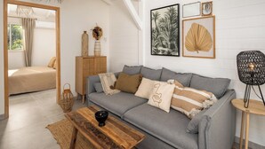A modern living room with a grey sofa, wooden coffee table, and a mirror. - Sweet Cane Tiny House & Pool (Saint-François)
