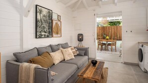 A cozy living room with a grey sofa, a wooden coffee table, and a dining area with a wooden table and chairs. - Sweet Cane Tiny House & Pool (Saint-François)