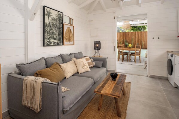 Ein gemütliches Wohnzimmer mit grauem Sofa, einem Holztisch und einem Essbereich mit Holztisch und Stühlen.