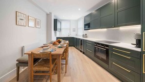 A modern kitchen with dark cabinets, a wooden dining table, and a breakfast setup. - Elegant split level High St Ken Apt with Terrace (London)