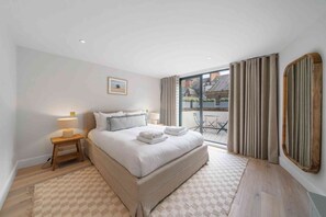 Une chambre d’hôtel avec un grand lit, une table de chevet avec une lampe, une vue sur l’extérieur par une fenêtre et un sol à carreaux.