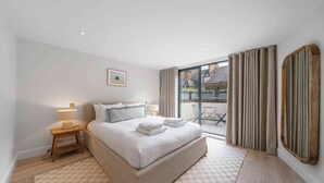 A bedroom with a large bed, a nightstand, a lamp, a view of the outside, and a window with curtains. - Elegant split level High St Ken Apt with Terrace (London)