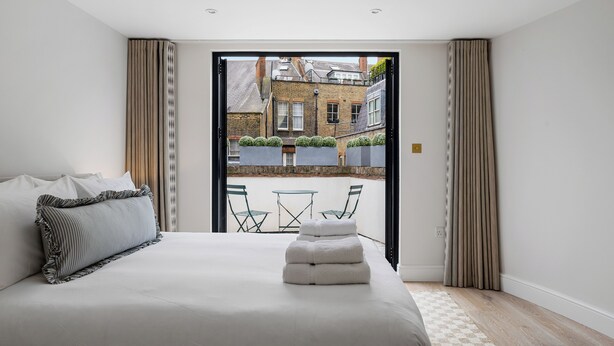 A bedroom with a large bed, a view of a courtyard, and a small table and chairs outside. - Elegant split level High St Ken Apt with Terrace (London)