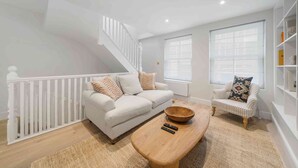 A modern living room with a white staircase, a white sofa, a striped armchair, and a wooden coffee table. - Elegant split level High St Ken Apt with Terrace (London)