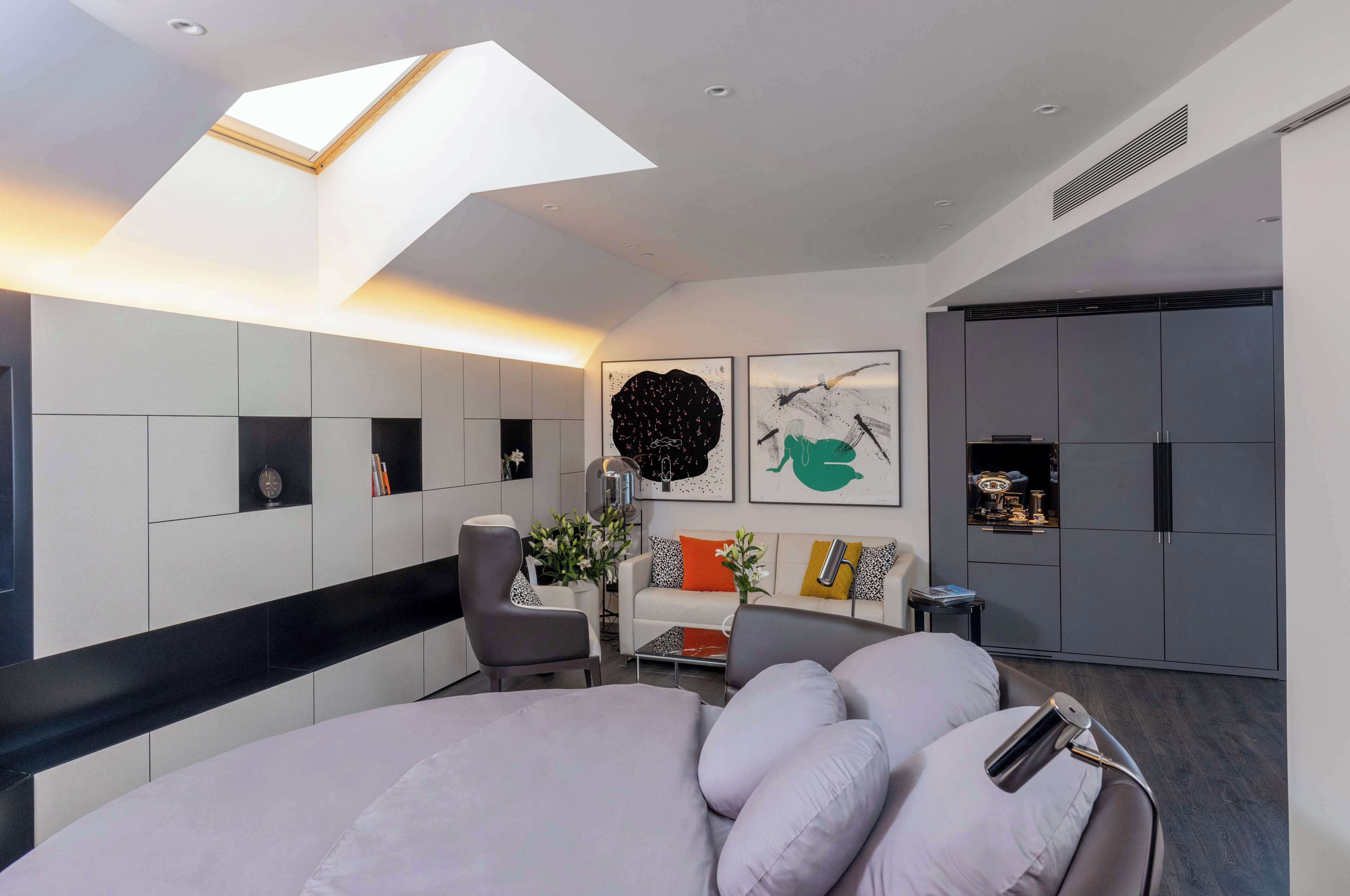 A modern bedroom with a skylight, grey wardrobe, and a bed with grey bedding.