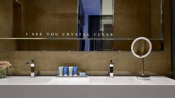 Un baño moderno con un espejo grande, un tocador con lavabo, y otro tocador con espejo. Hay tres botellas de loción sobre el tocador.
