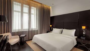 A modern hotel room with a large bed, a desk, a chair, and a nightstand with lamps.