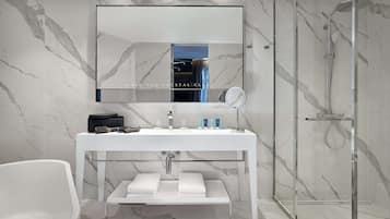 Un baño moderno con pared de mármol, cabina de ducha de vidrio, tocador blanco con espejo y bañera.