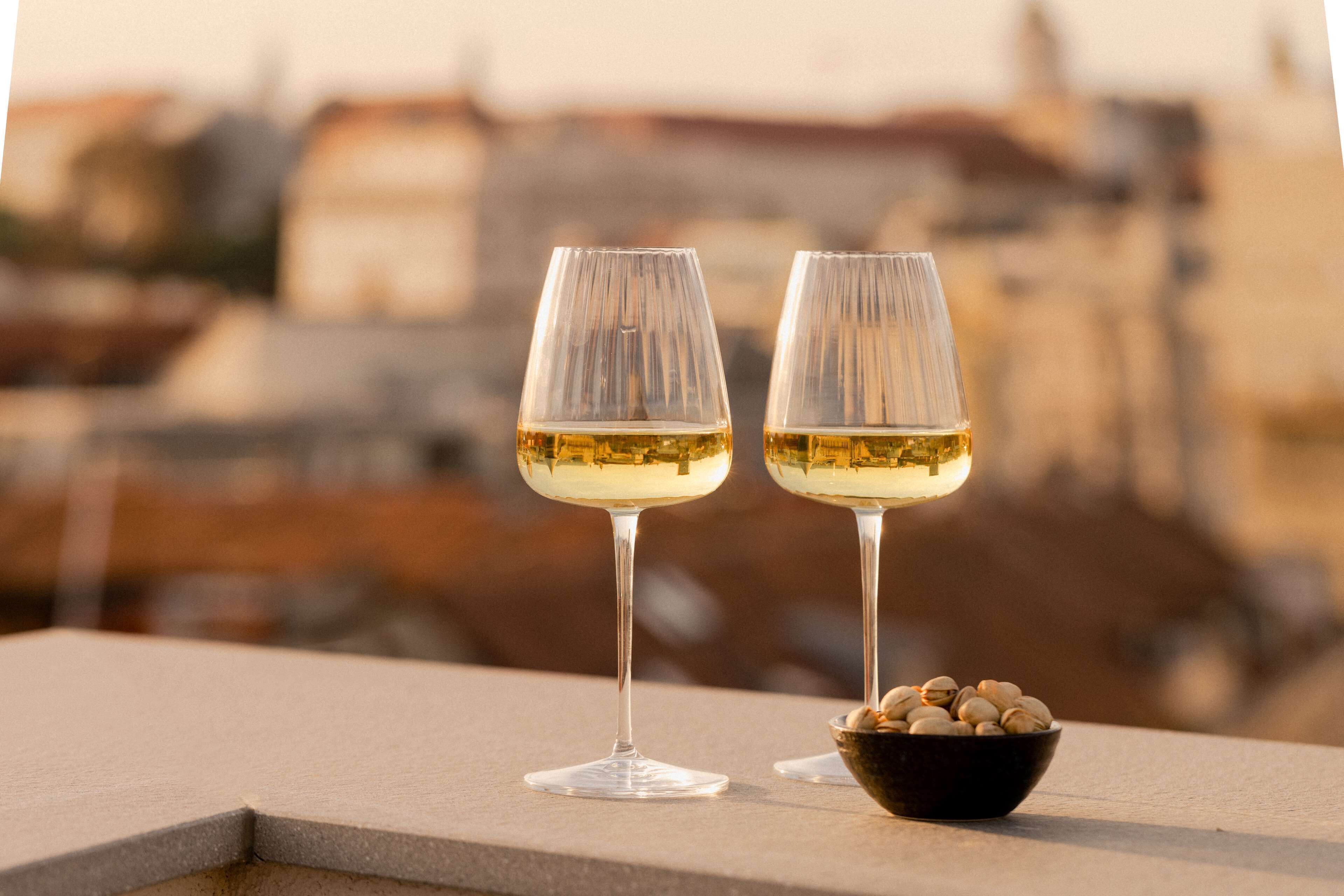 Two glasses of white wine on a balcony with a bowl of nuts.
