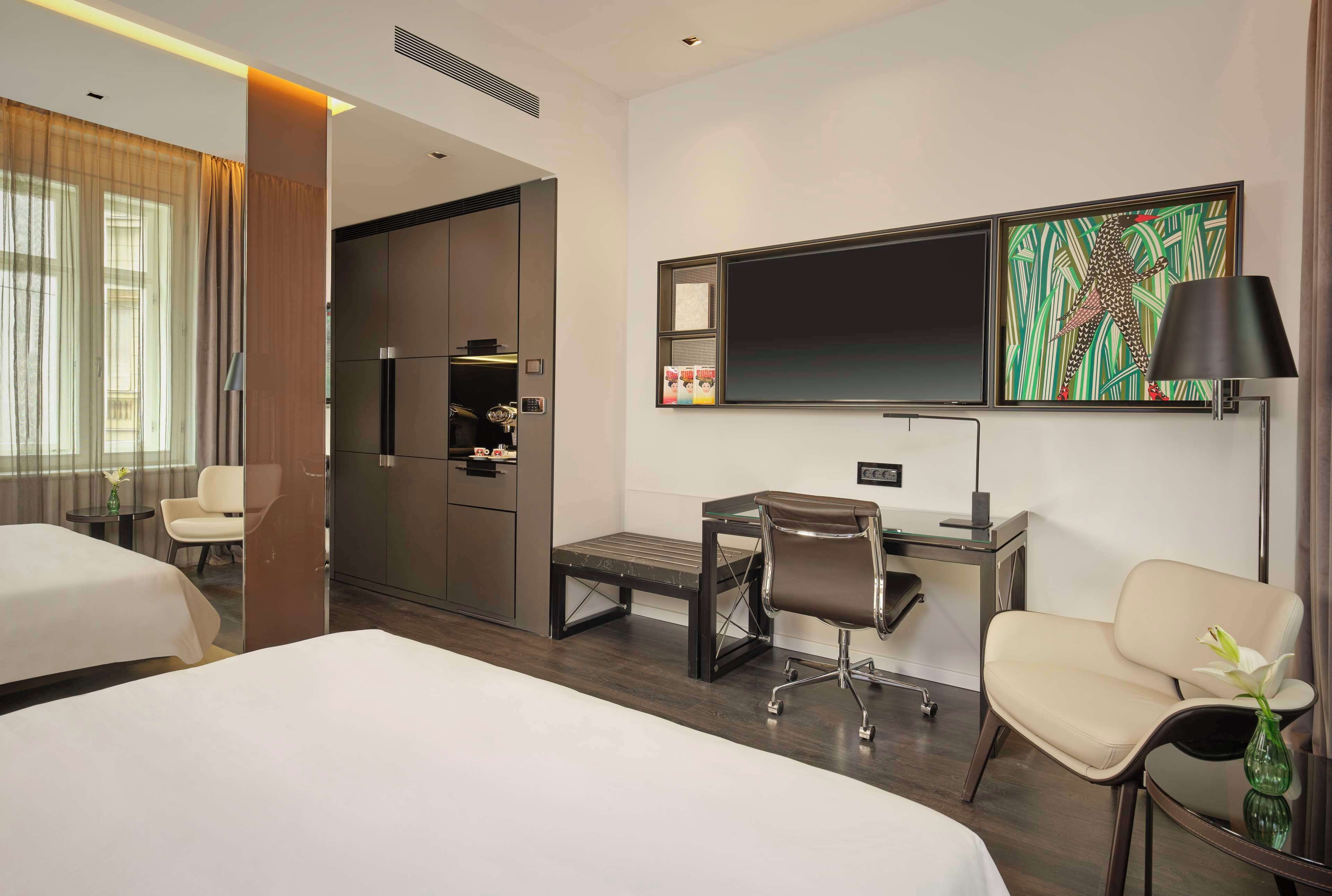 A hotel room with two beds, a desk with a chair, a TV, and artwork on the wall.
