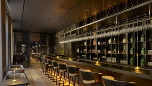Een moderne bar met een lange toonbank, meerdere stoelen en diverse glazen en flessen op planken.