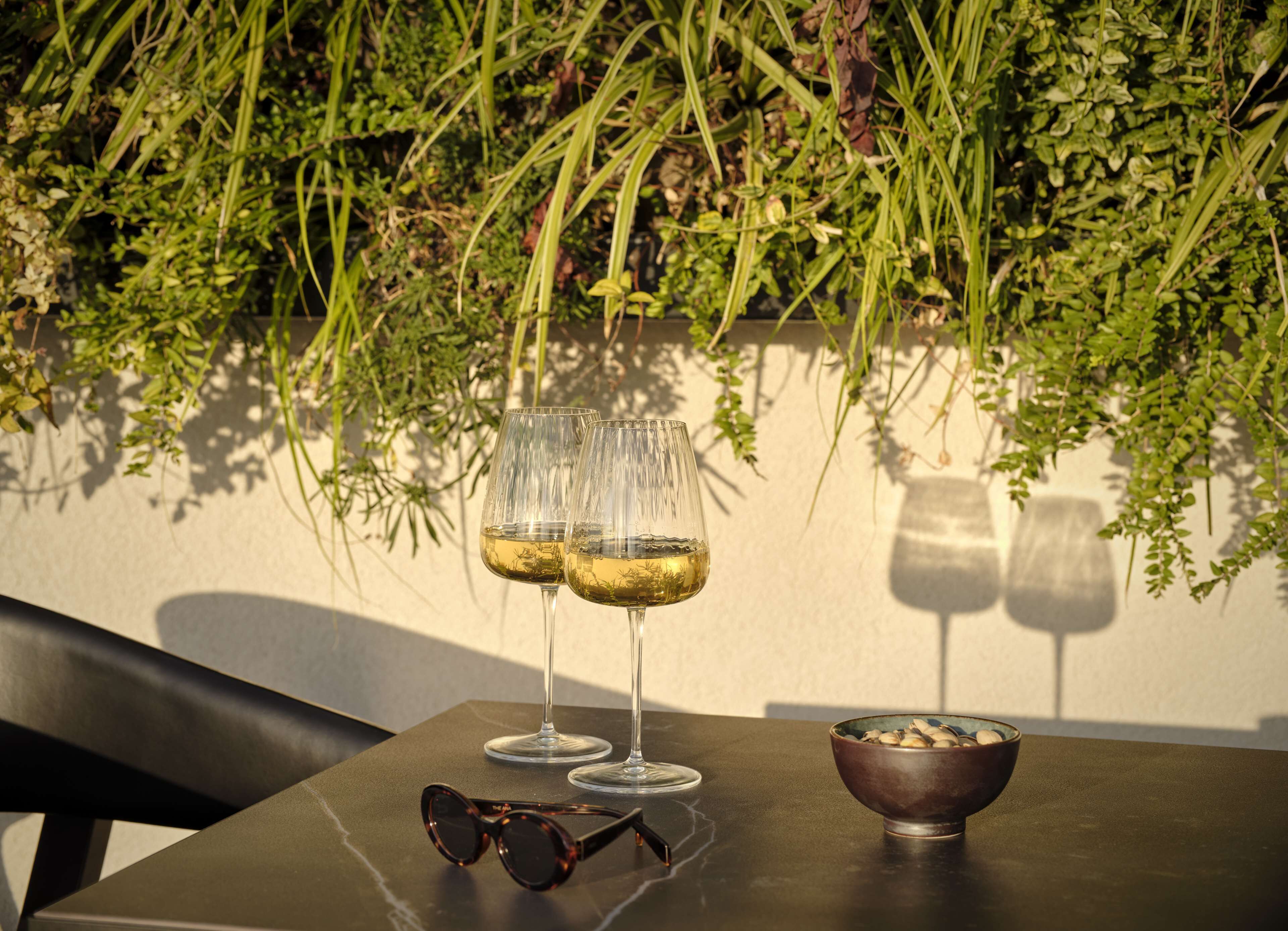 A table with two wine glasses, a pair of sunglasses, and a bowl of nuts.